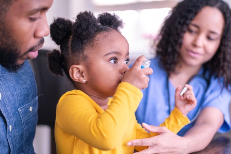 Two parents with a young child using an inhaler