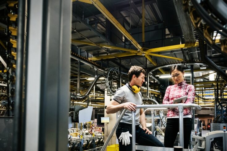 Mechanic and manager talking nearby a machine in a big printery about latest newspaper print