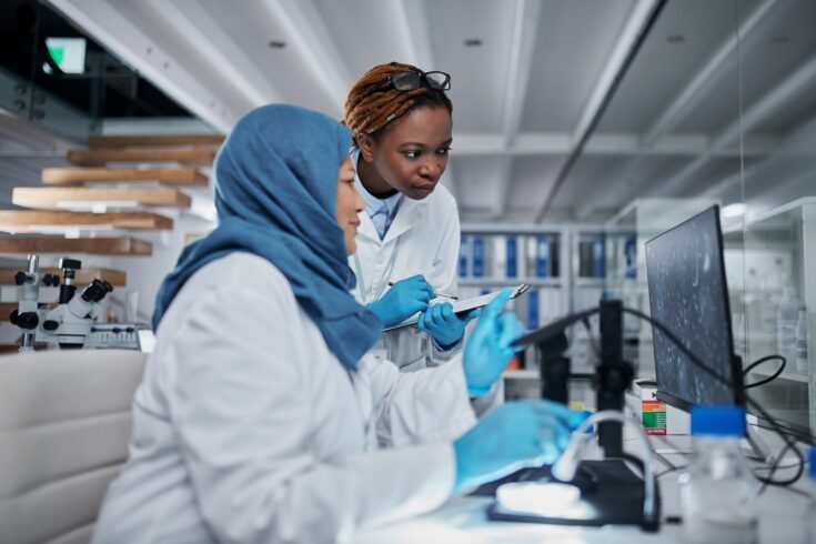 Two female scientists working with a computer and a digital microscope in a laboratory