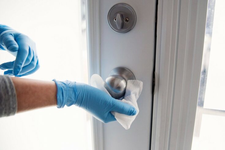 Gloved hands cleaning a door handle