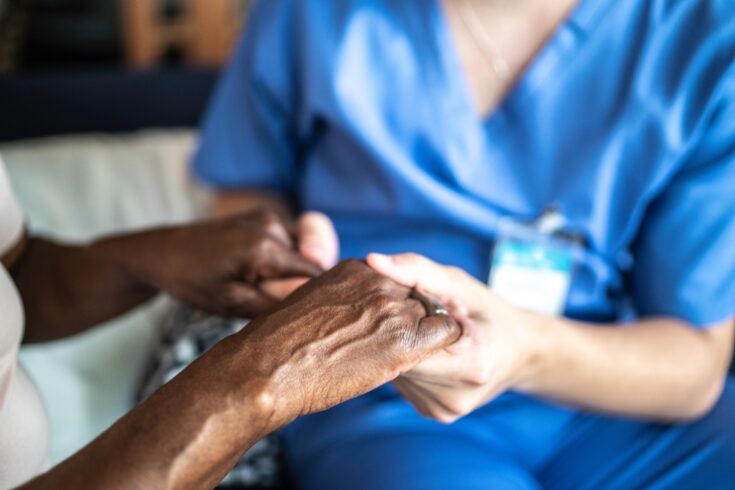 Close-up of healthcare worker and senior woman holding hands