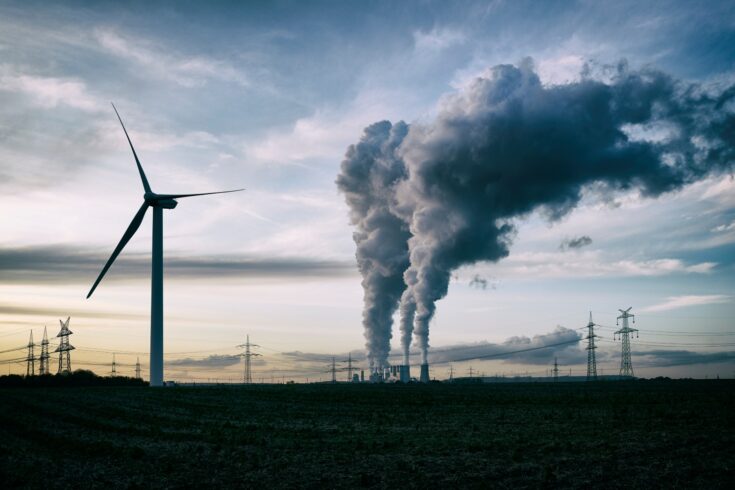 Single wind turbine, a coal burning power plant with pollution and electricity pylons in the background