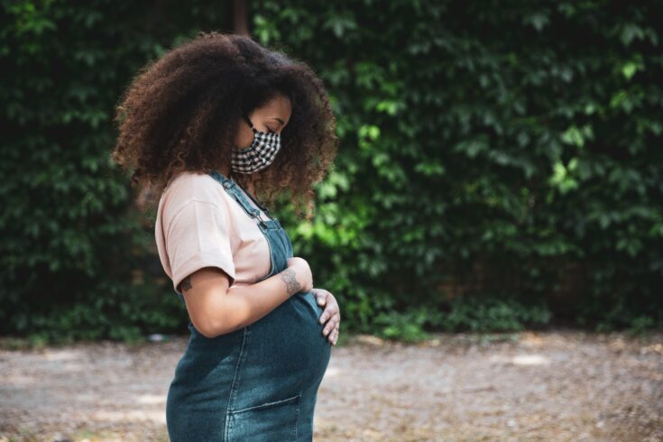 A pregnant woman outside wearing a protective face mask