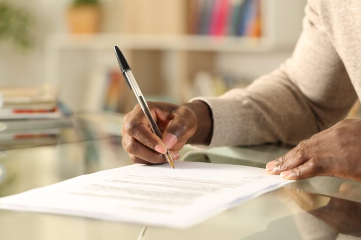 Close up of black man hands signing document on a desk