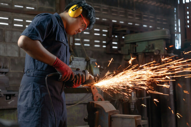 Asian Mechanical engineer operating power tools with metal sparks