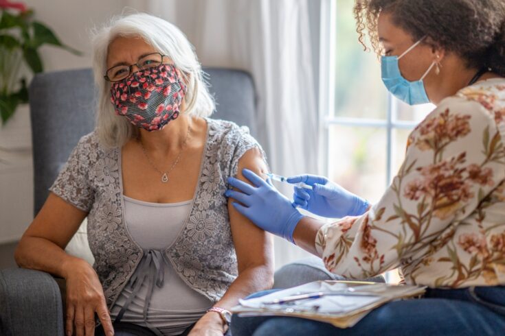 Senior woman getting a vaccine from her doctor in her home during a house visit during the COVID-19 pandemic