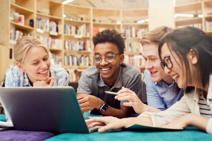 Diverse students looking at a laptop in a library
