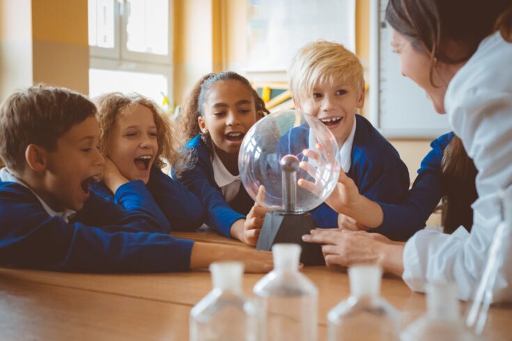 Group of school kids listening to female teacher showing plasma ball during physics lesson