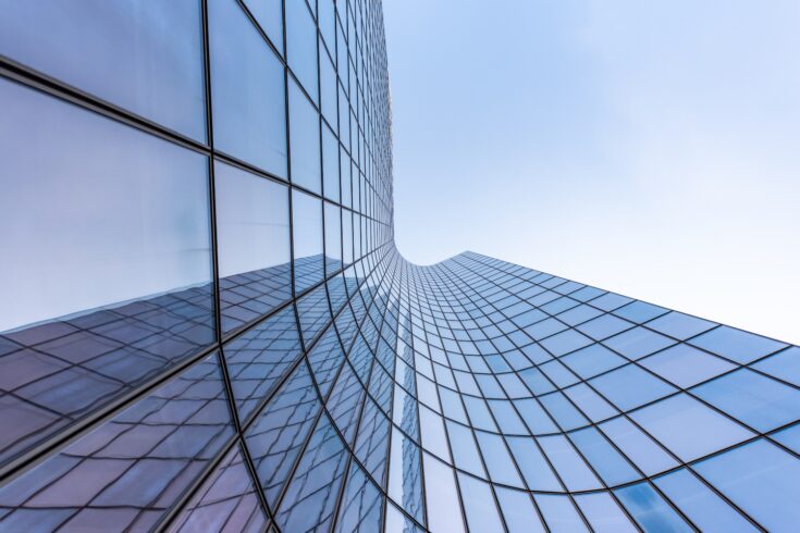 Blue curved glass skyscraper facade reflections against sky