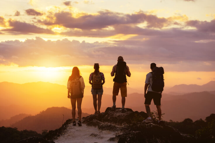 Four people's silhouettes on mountain top looks at sunset