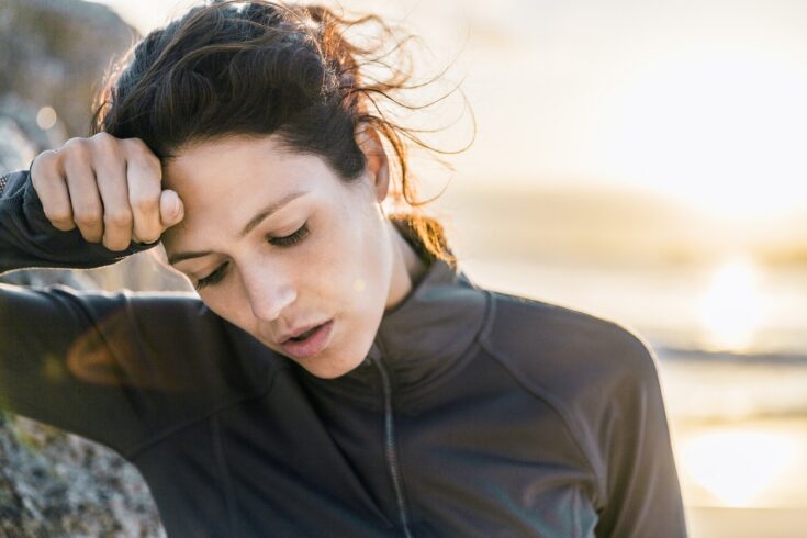 Exhausted athlete is wiping forehead at beach