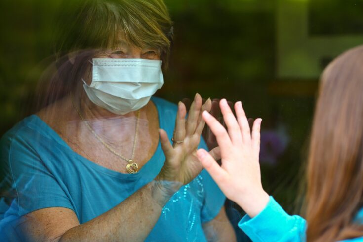 Grandmother and granddauther touch hands on window while on visit