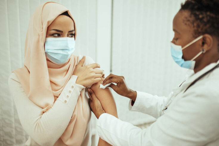 African American female doctor is giving flu or coronavirus vaccine to Arabian female.