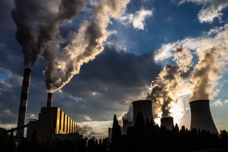 View of the smoking chimneys of a coal-fired power plant against the backdrop of a dramatic sky with clouds