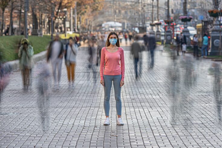 Woman with medical face mask stands on the crowded street