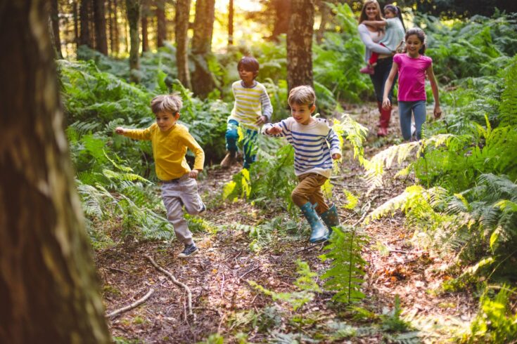 Group of children at running through a woodland with their guide/teacher walking behind them