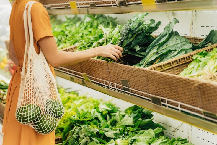 Girl is holding mesh shopping bag with vegetables without plastic bags at grocery shop.