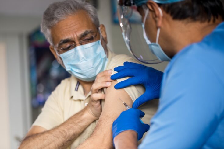 Doctor injecting vaccine into arm of senior male patient