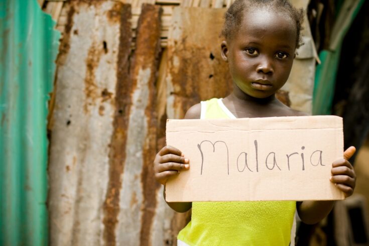 An African girl holding a sign with 'Malaria' written on it