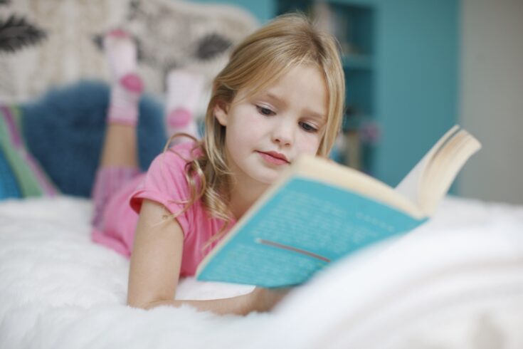 Girl lying on bed reading book