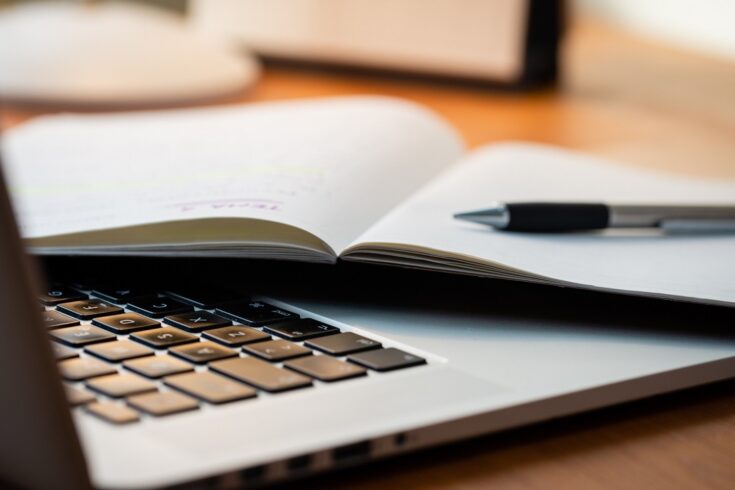 Laptop next to a notebook and pen