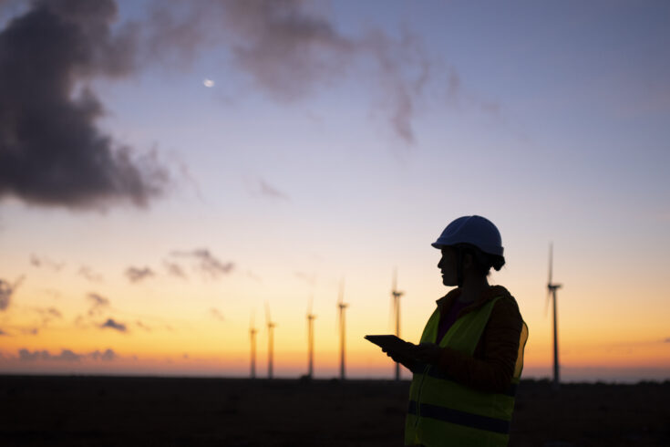 Renewable Energy Systems. Electricity Maintenance Engineer working on the field at a Wind Turbine Power station at dusk.