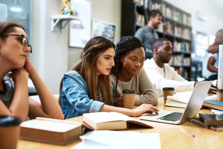 Two women using a laptop together in a college library