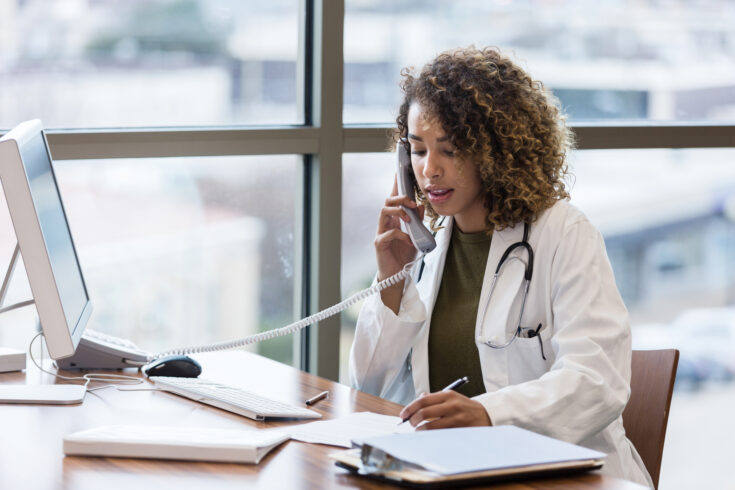 Mid adult female doctor makes phone call regarding patient records