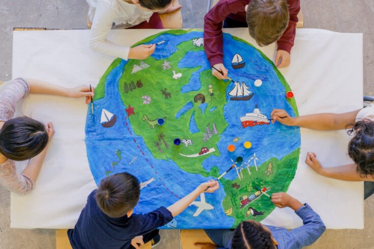 An aerial view of a multi ethnic group of children painting the globe and it's animals, fish, and vehicles