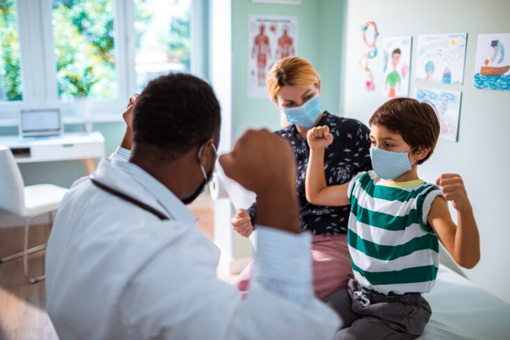 A child talks to a doctor in his office, with his parents in the background