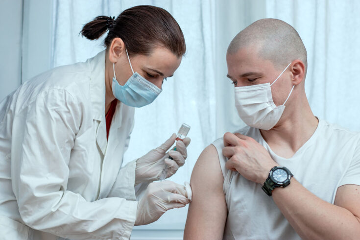 Female doctor preparing to inject male patient with COVID-19 antiviral vaccine.