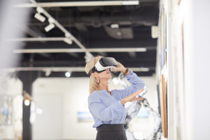 Woman wearing virtual reality headgear while enjoying immersive experience during exhibition in art gallery