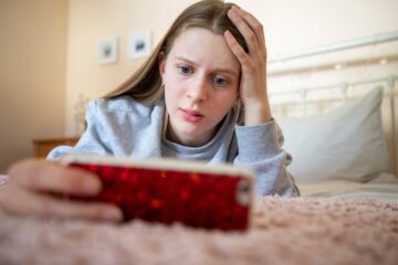 Worried teenage girl lying on bed with mobile phone