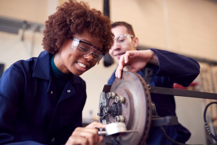 Male And female students working on car brakes on auto mechanic apprenticeship course at college