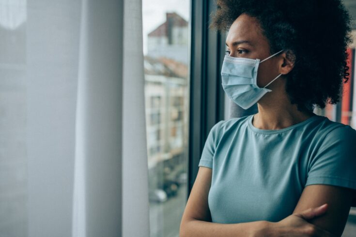 Worried young woman looking through window at home in quarantine