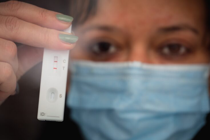 Masked woman holding positive COVID-19 lateral flow test at home