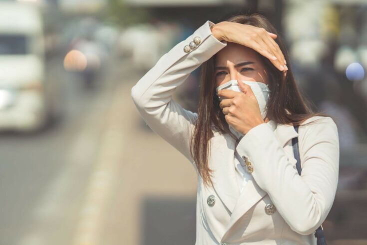 Woman holding a mask to her face to avoid traffic air pollution