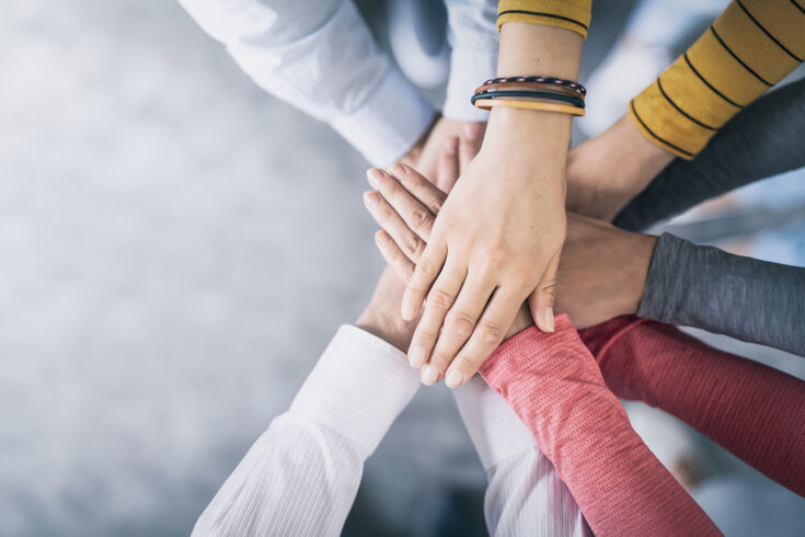 Close up top view of young business people putting their hands together.