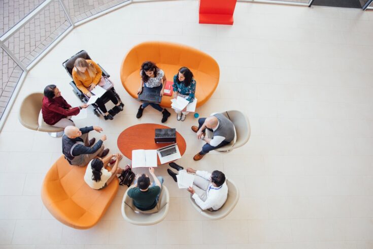 A birds-eye view of an academic group meeting in natural light with bright furniture