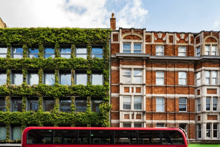 A vertical garden exterior contrasting with old and new building architecture and red London bus