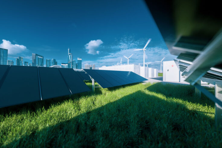 Modern black frameless solar panel farm, battery energy storage and wind turbines on fresh green grass under blue sky.