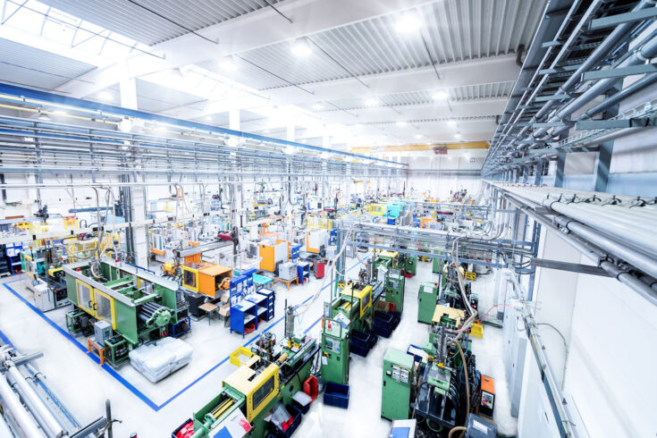 Industrial aisle surrounded by modern machines which having busy robotic arms with molding shapes and producing plastic pieces for variety of industry. Labor intensive production line with manufacturing equipment: boxes, crates, crane, packages, pallets, space for copy.
