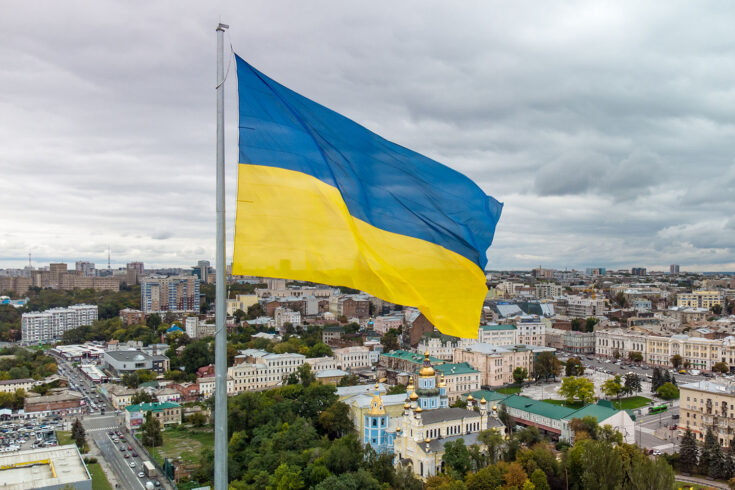 Flag of Ukraine waving with epic gray cloudscape, autumn city aerial view near river Lopan embankment, Svyato-Pokrovskyy Monastyr in Kharkiv, Ukraine.