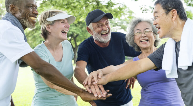 A diverse group of senior people joining hands and smiling at each other