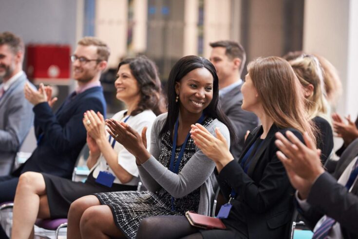 A diverse group of audience clapping and smiling in a conference setting