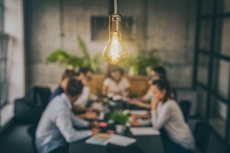 Young business people are discussing together a new startup project with a glowing light bulb in the foreground