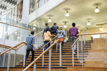 Male and female college students in casual clothing, on way to class, ascending staircase.