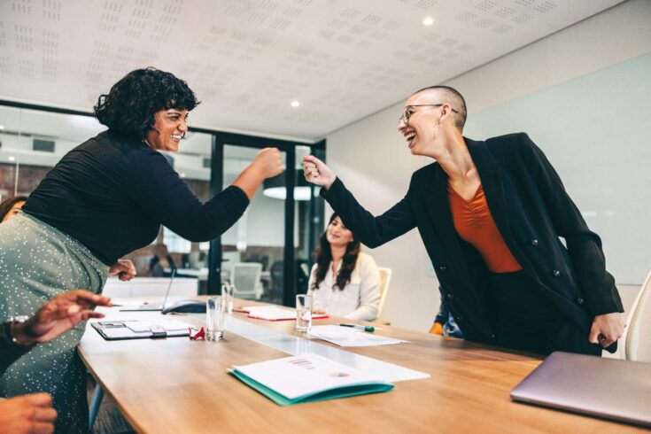 Two businesswomen fistbumping each other in a meeting room