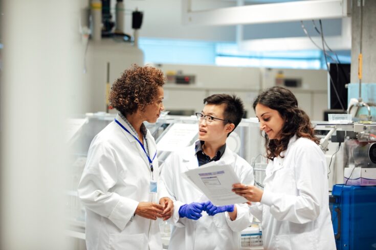 Diverse mix of technicians, wearing lab coats, debate working procedure, in a disease research facility