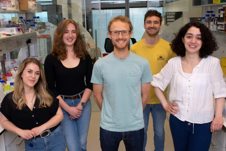 Dr Joe Yeeles and his team smiling, standing in a lab.